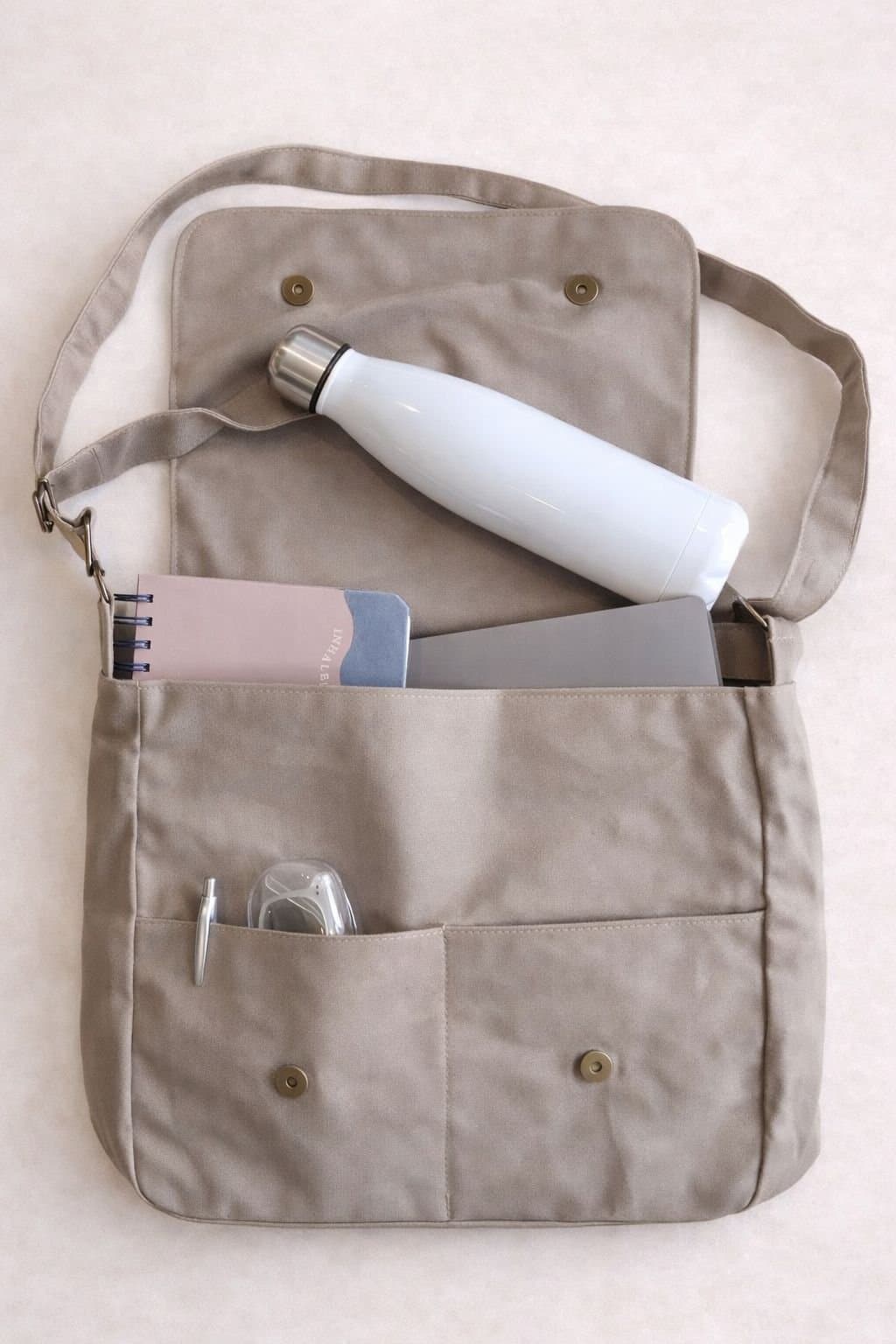 Morral Beige V1 abierto, con una botella, un cuaderno y lapiceras en los bolsillos