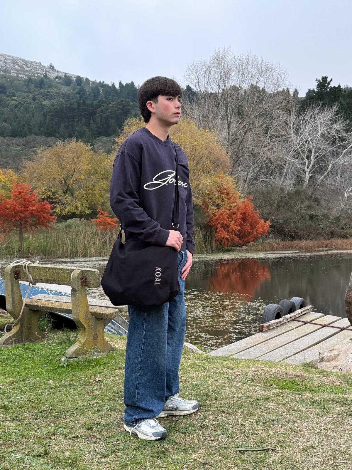 Morral Negro V2 al hombro, de cuerpo entero junto a un lago